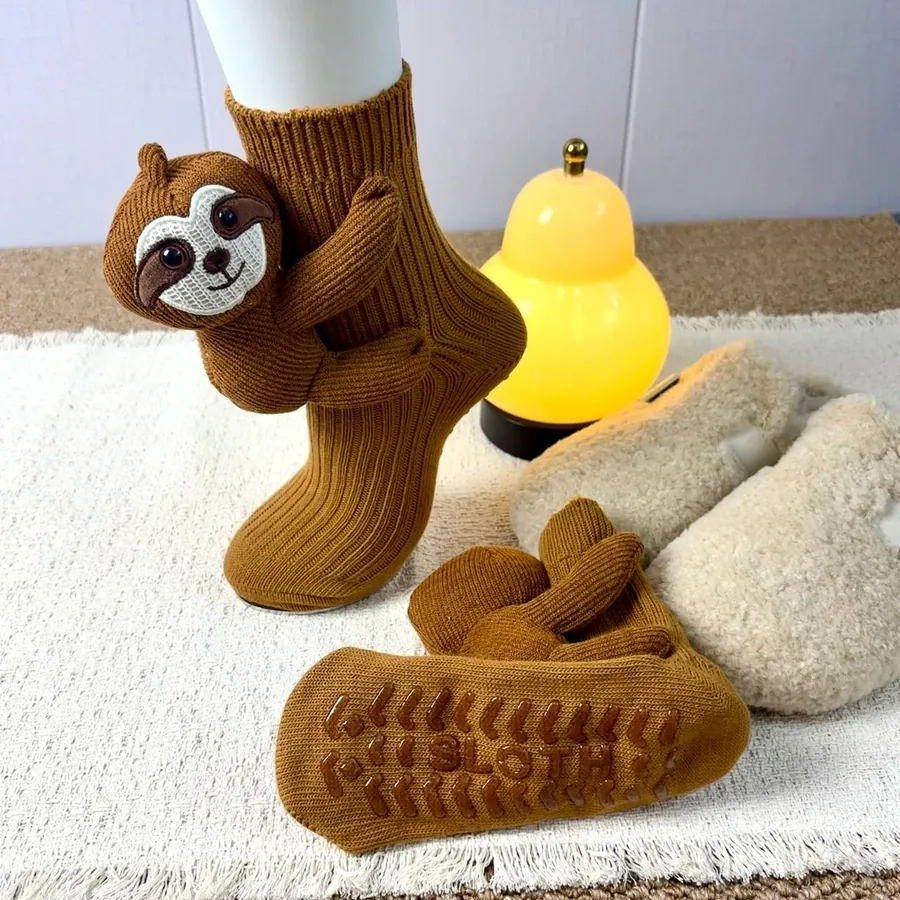 Sloth animal socks showing the ribbed knit and textured grip sole beside a soft throw